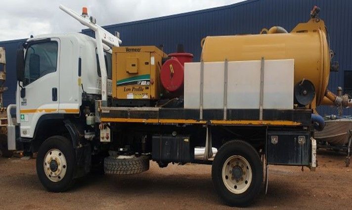 White truck with yellow tank and equipment, parked in front of a blue building.