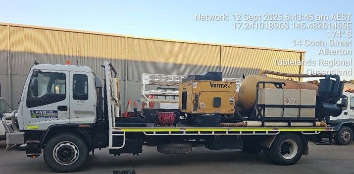 Truck with equipment, in Atherton, Australia. Yellow building, blue sky.