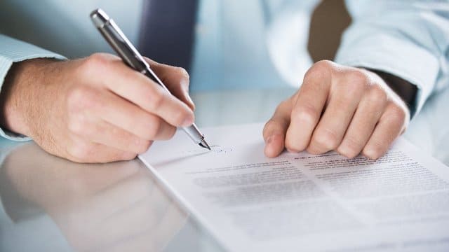Ein Mann schreibt mit einem Stift auf ein Blatt Papier.