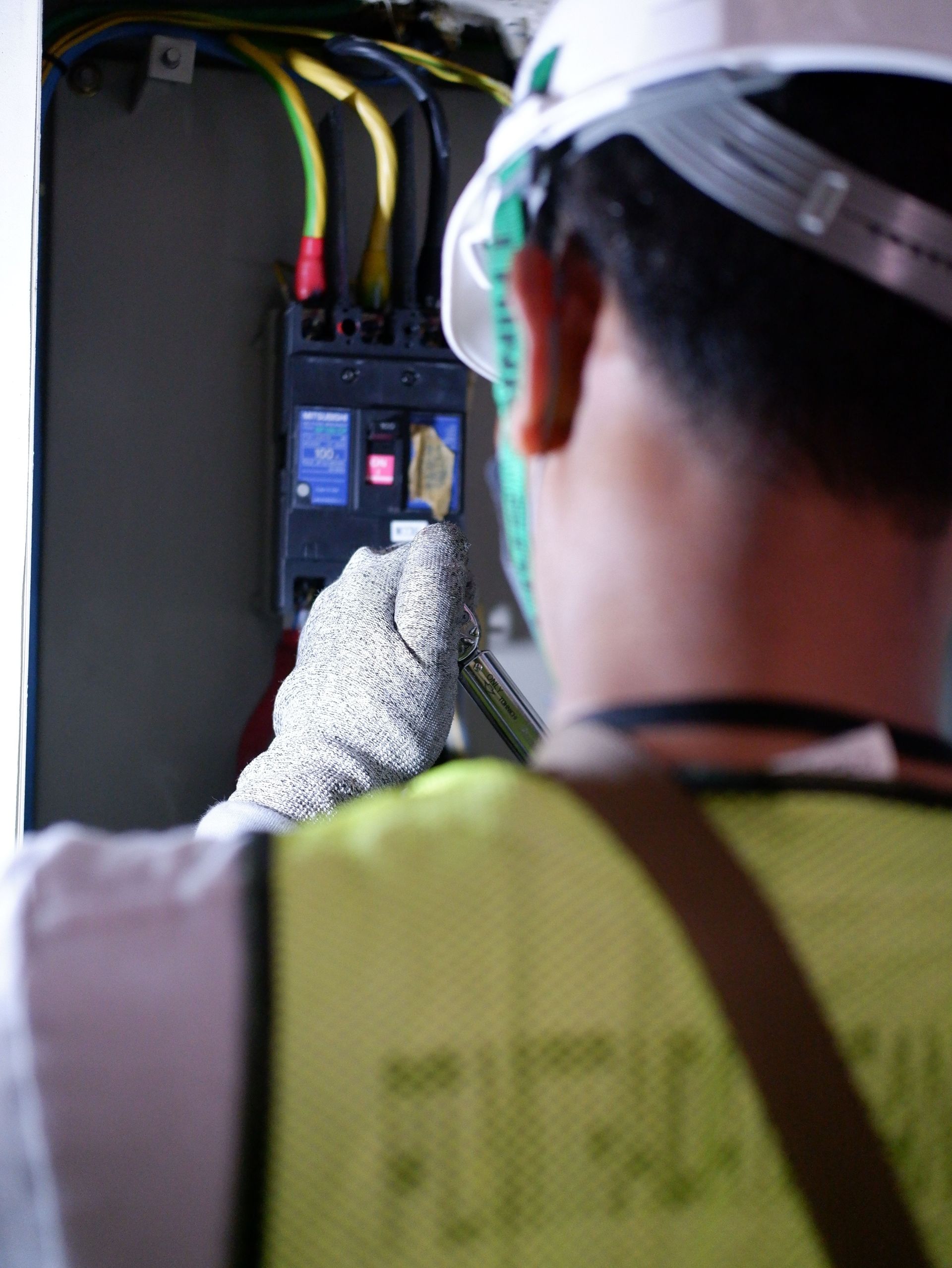 Worker inspecting an electrical panel with gloved hands in a utility cabinet