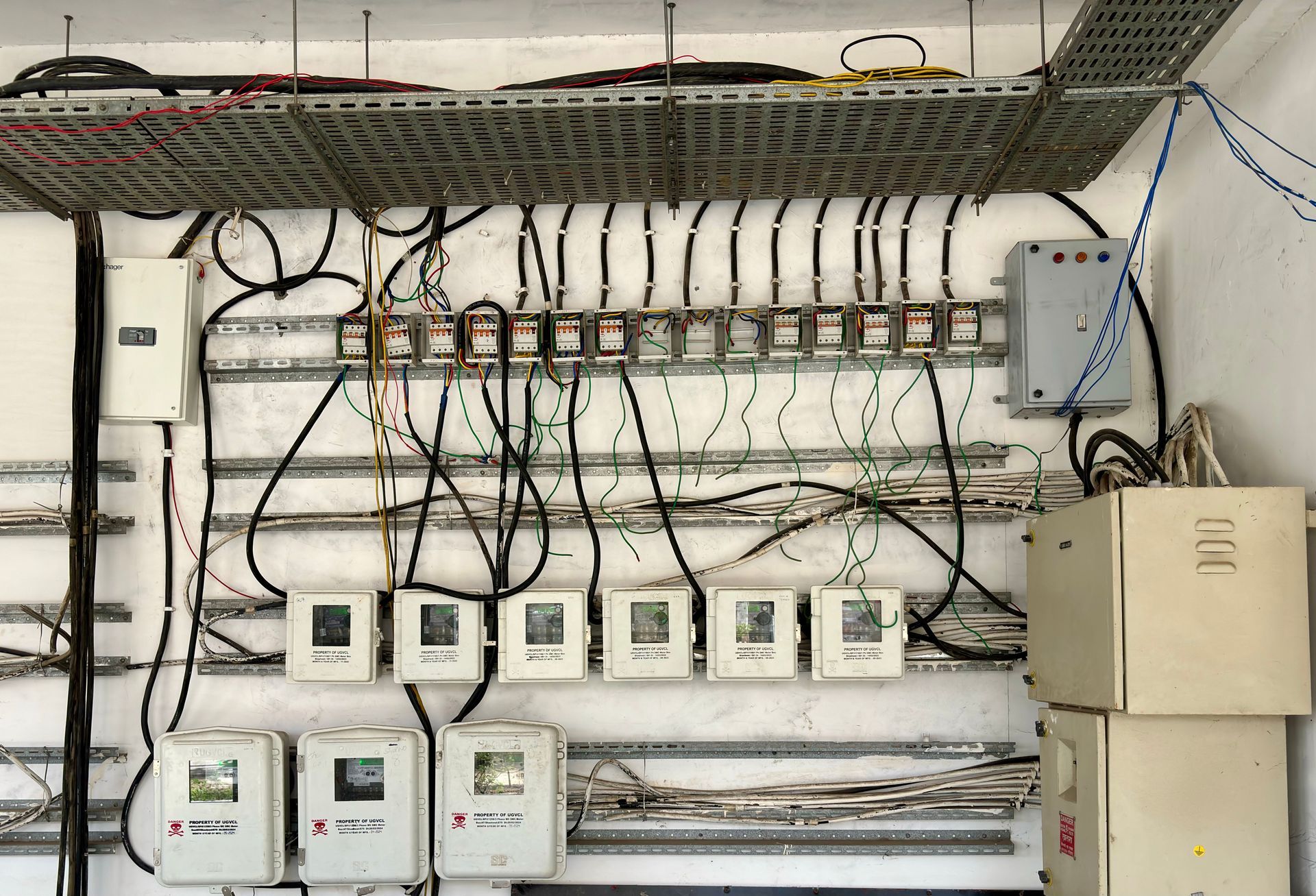 Wall-mounted electrical control panel with wiring, switches, meters, and conduit in a utility room