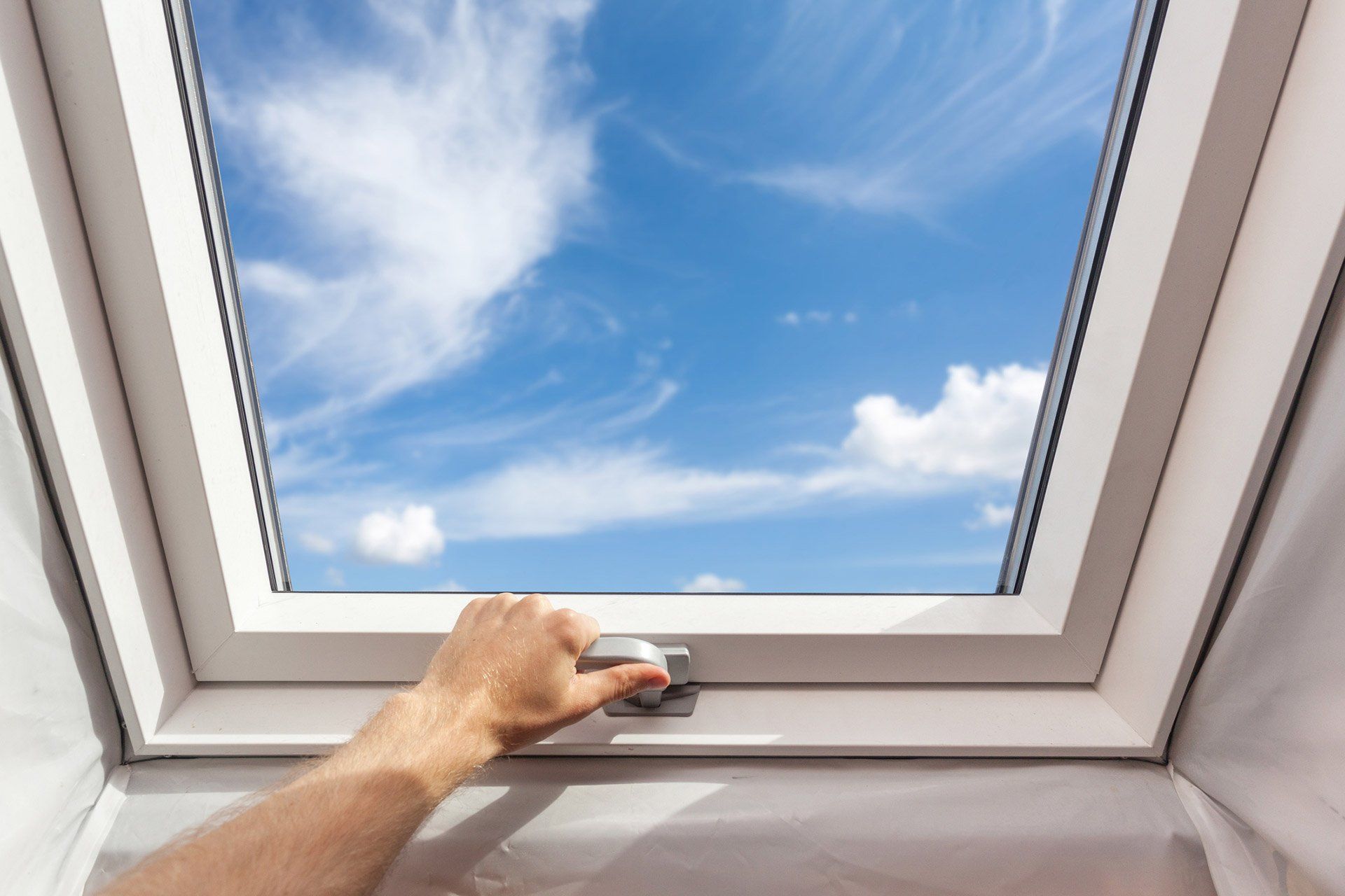 a person is opening a skylight with a blue sky in the background