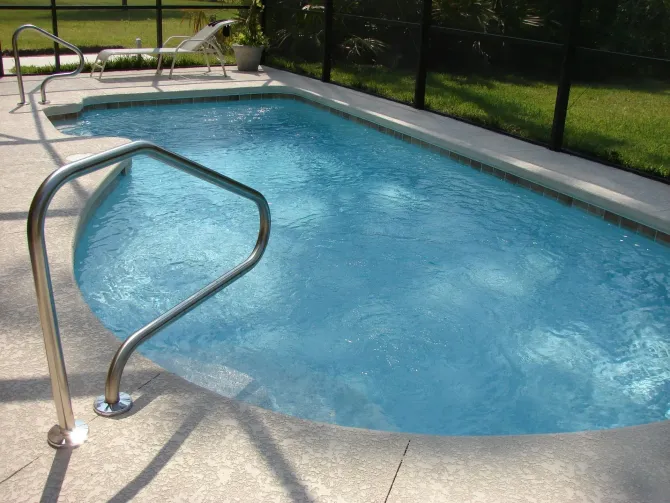 Screened-in backyard pool with metal handrails.
