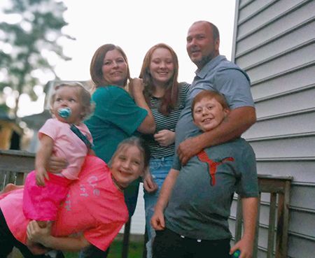 Family of six posing outdoors on a deck; two young girls, boy, teen girl, two adults.