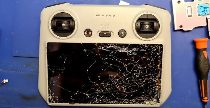 Un mando a distancia roto está sobre una mesa azul junto a un destornillador.