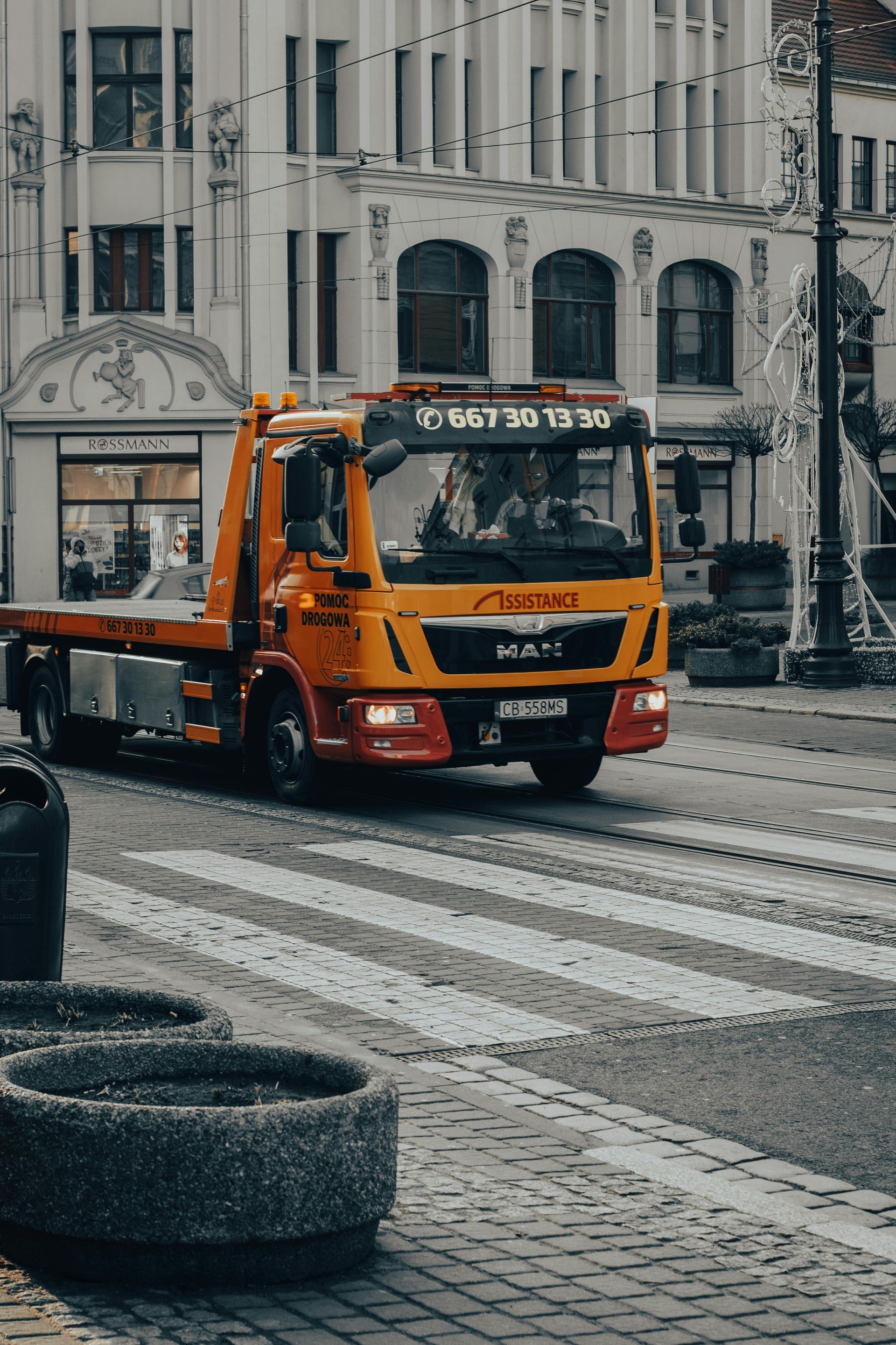 Orange tow truck on a crosswalk in front of a building with decorative details.