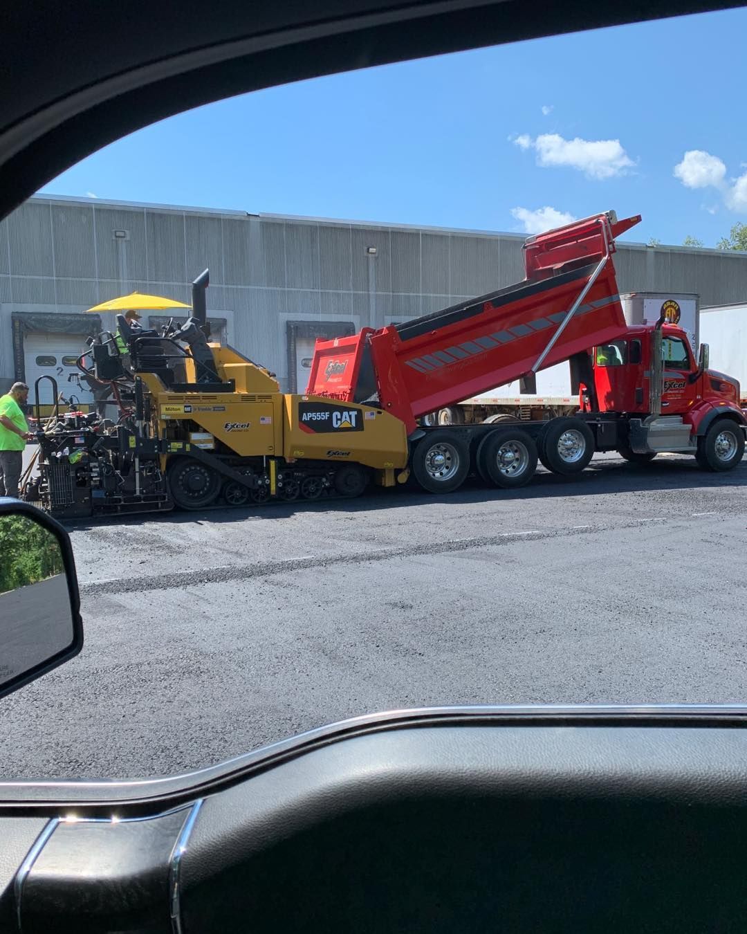 A dump truck is being loaded with asphalt in a parking lot.