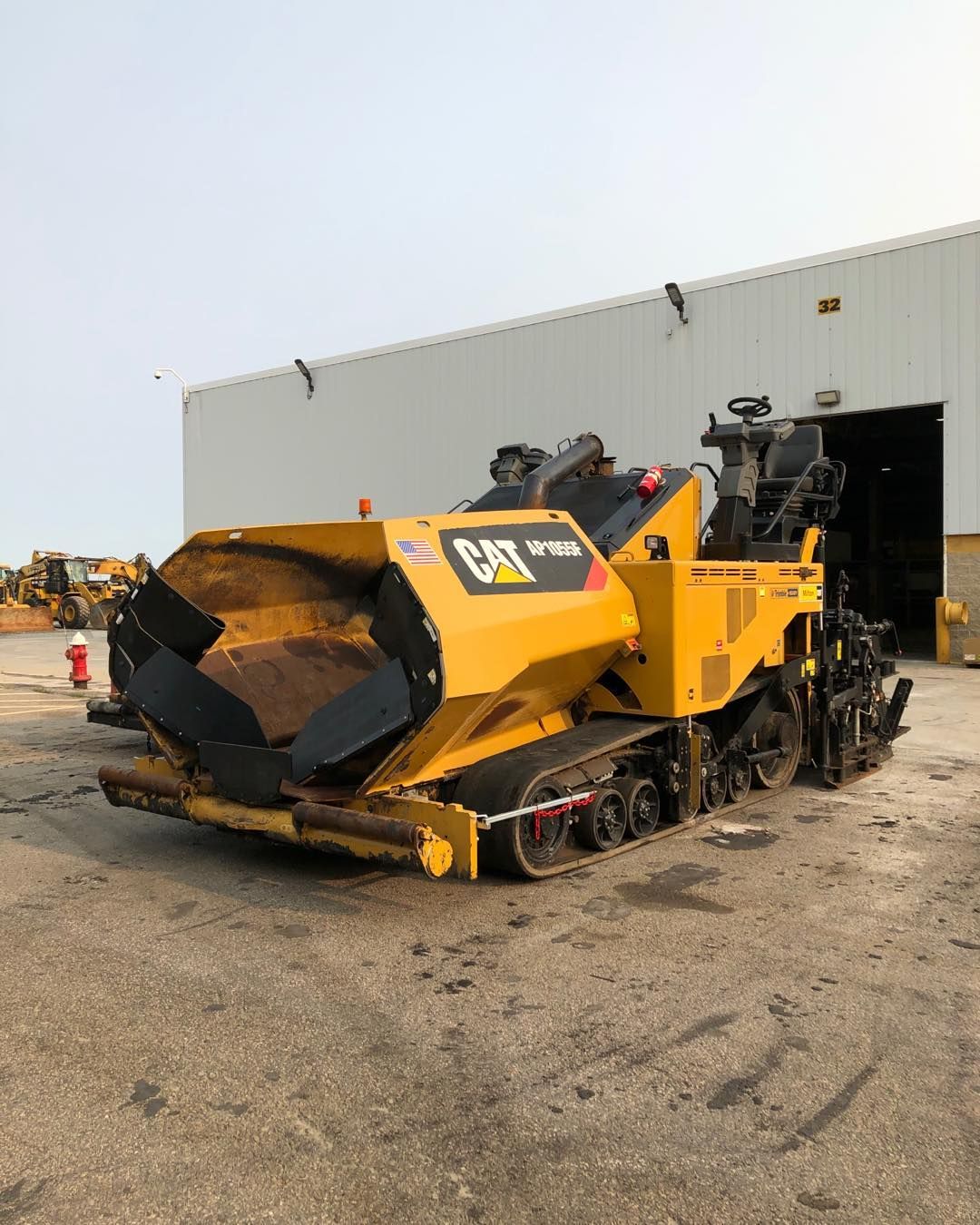 A yellow cat asphalt paver is parked in front of a building.