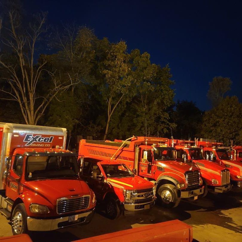 A row of red trucks are parked in a parking lot at night.