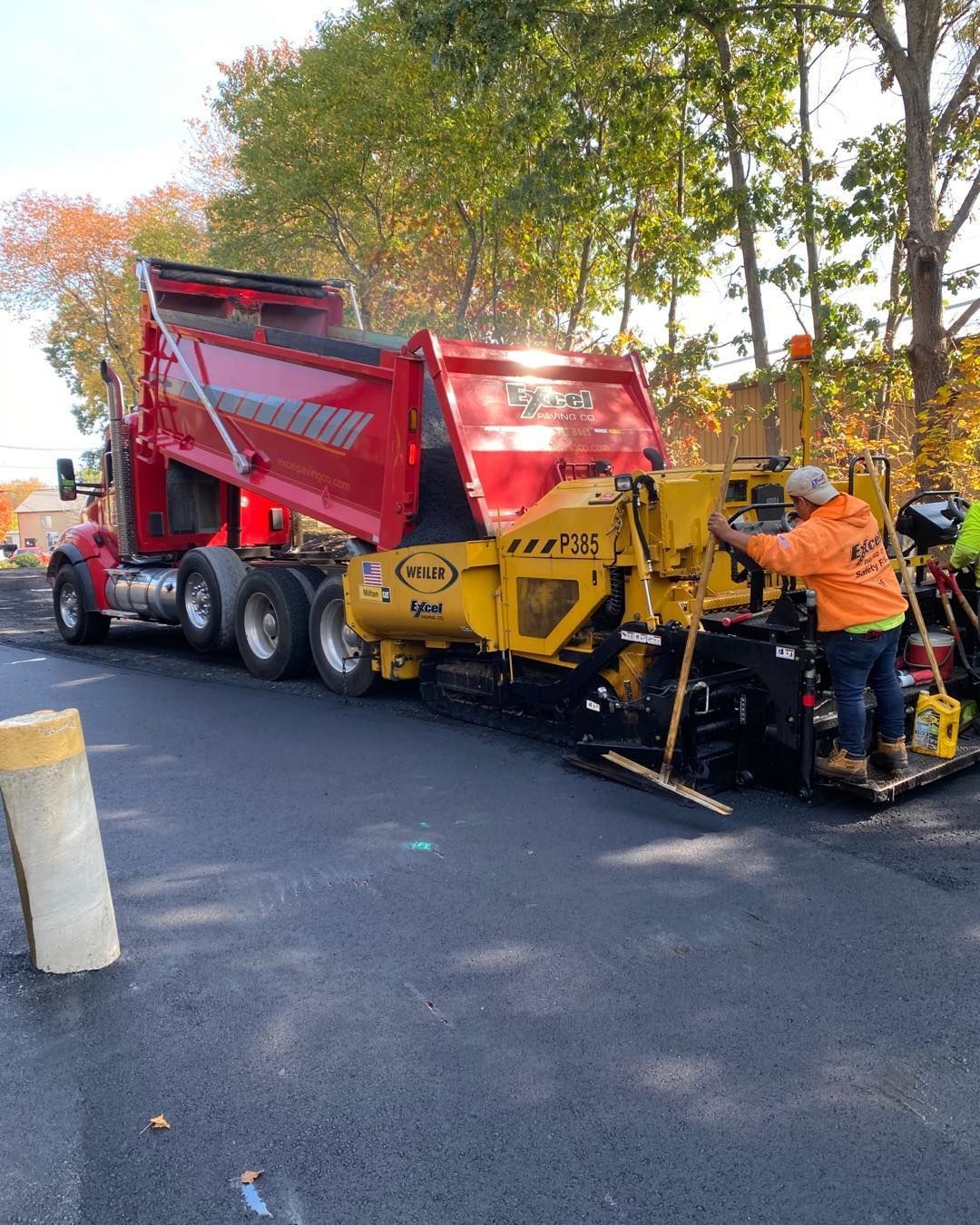 A man is sitting on a machine next to a dump truck.