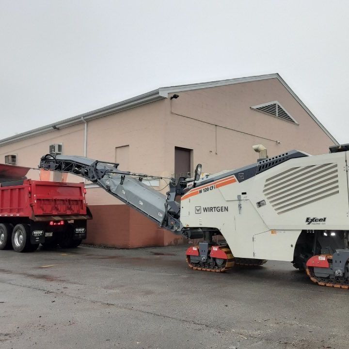 A red dump truck is parked next to a white machine that says artisan