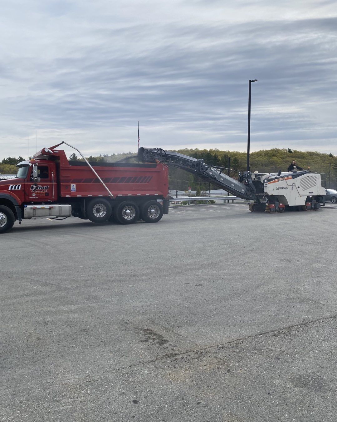 A red dump truck is parked next to a machine in a parking lot.
