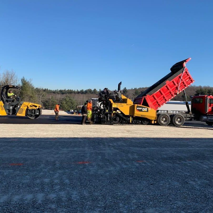 A dump truck is being loaded with asphalt on a construction site.
