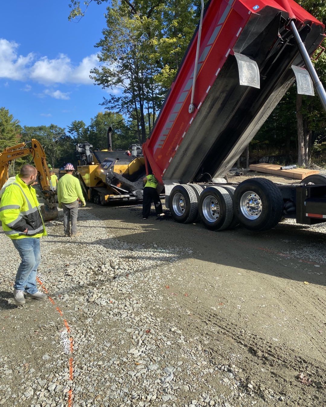 A dump truck is being loaded with gravel on a dirt road.