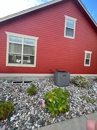 Red-sided house with white-trimmed windows; air conditioner on a bed of river rock in front of the house.