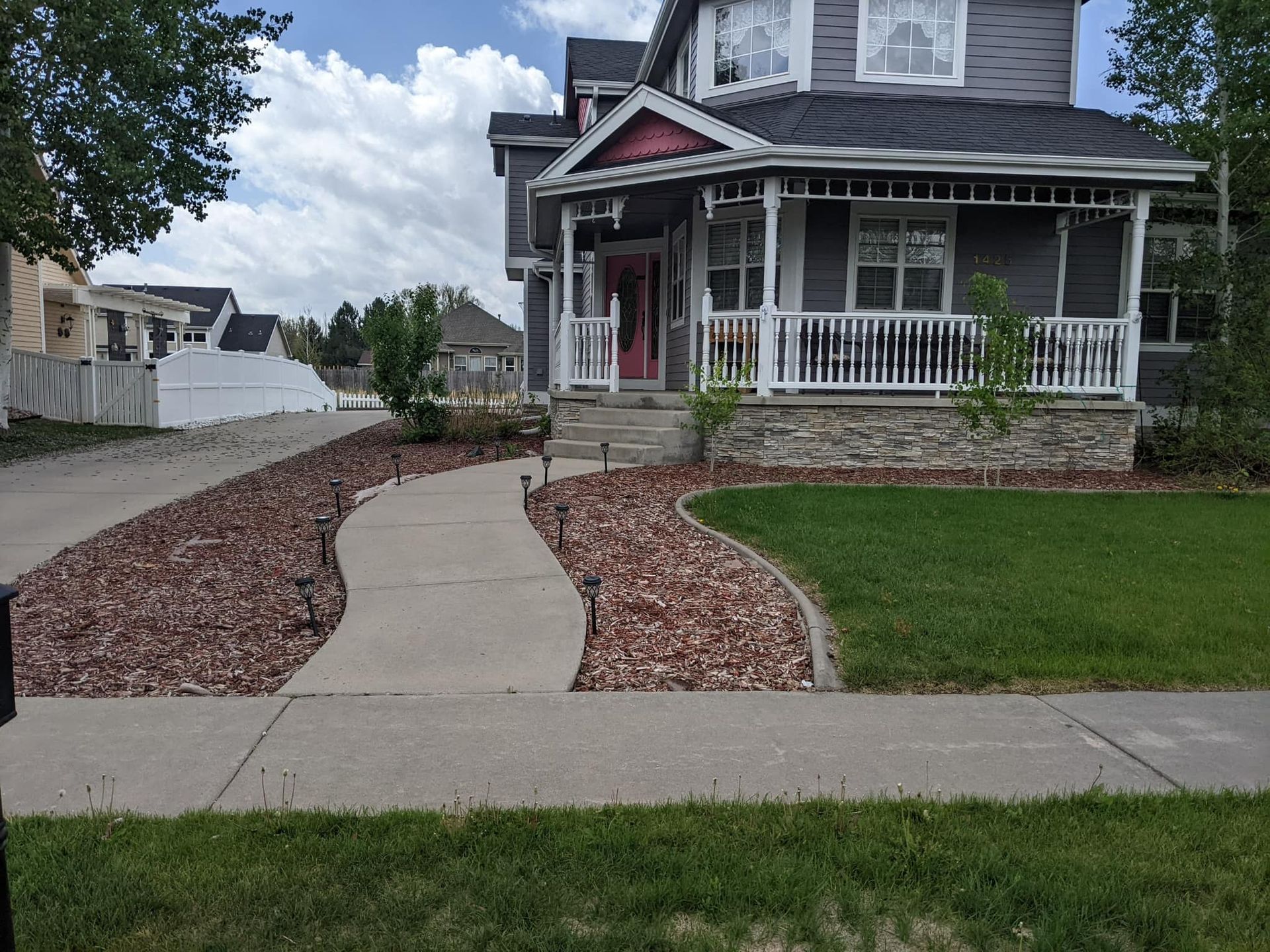 Gray house with porch, concrete walkway, and landscaped yard.