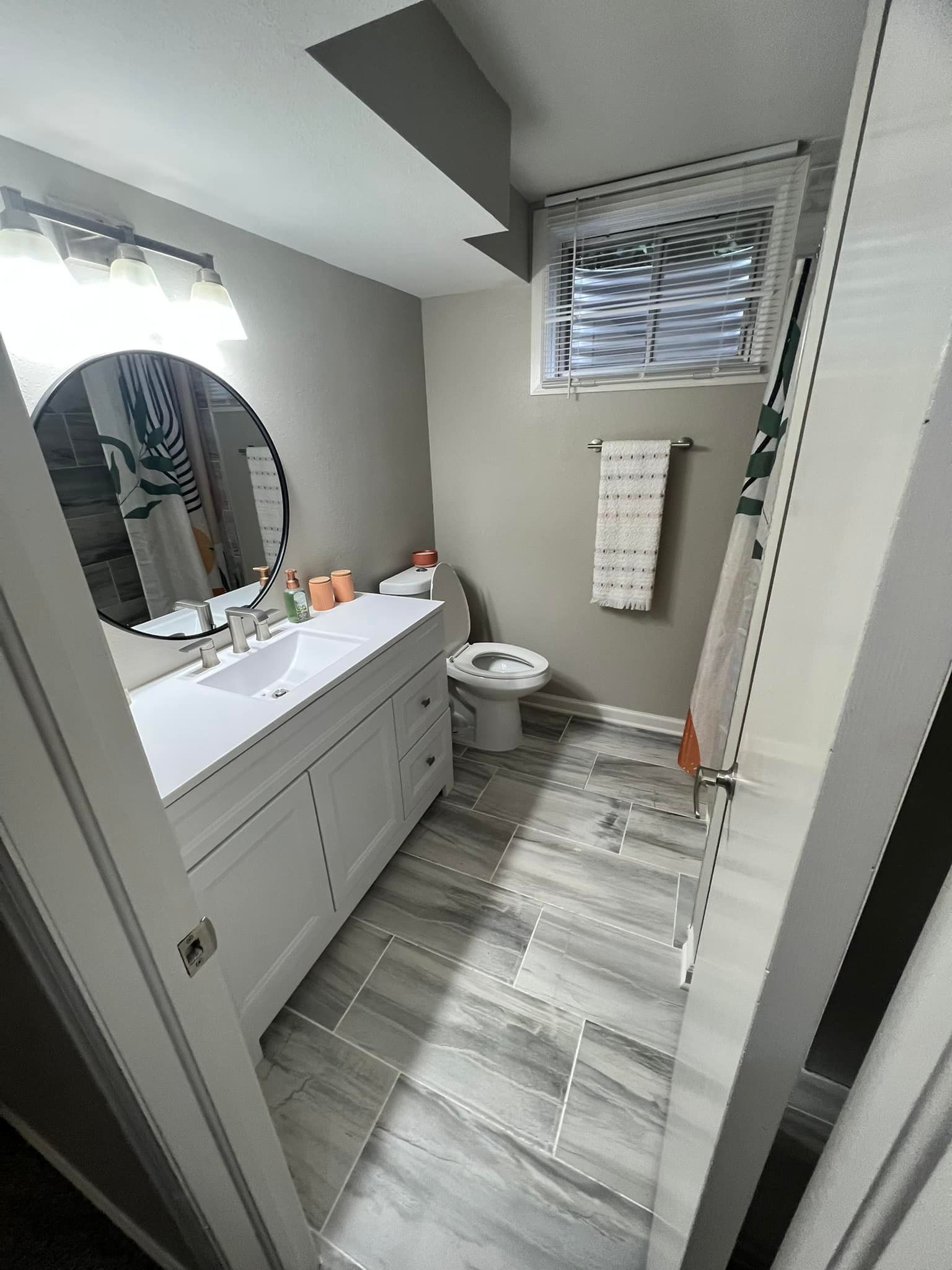 White bathroom with vanity, toilet, and window with a towel rack.