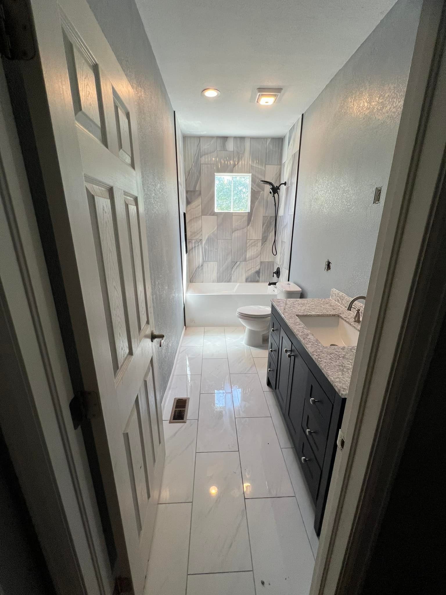Narrow bathroom with white tile floor, vanity, toilet, tub, and mosaic tile walls.
