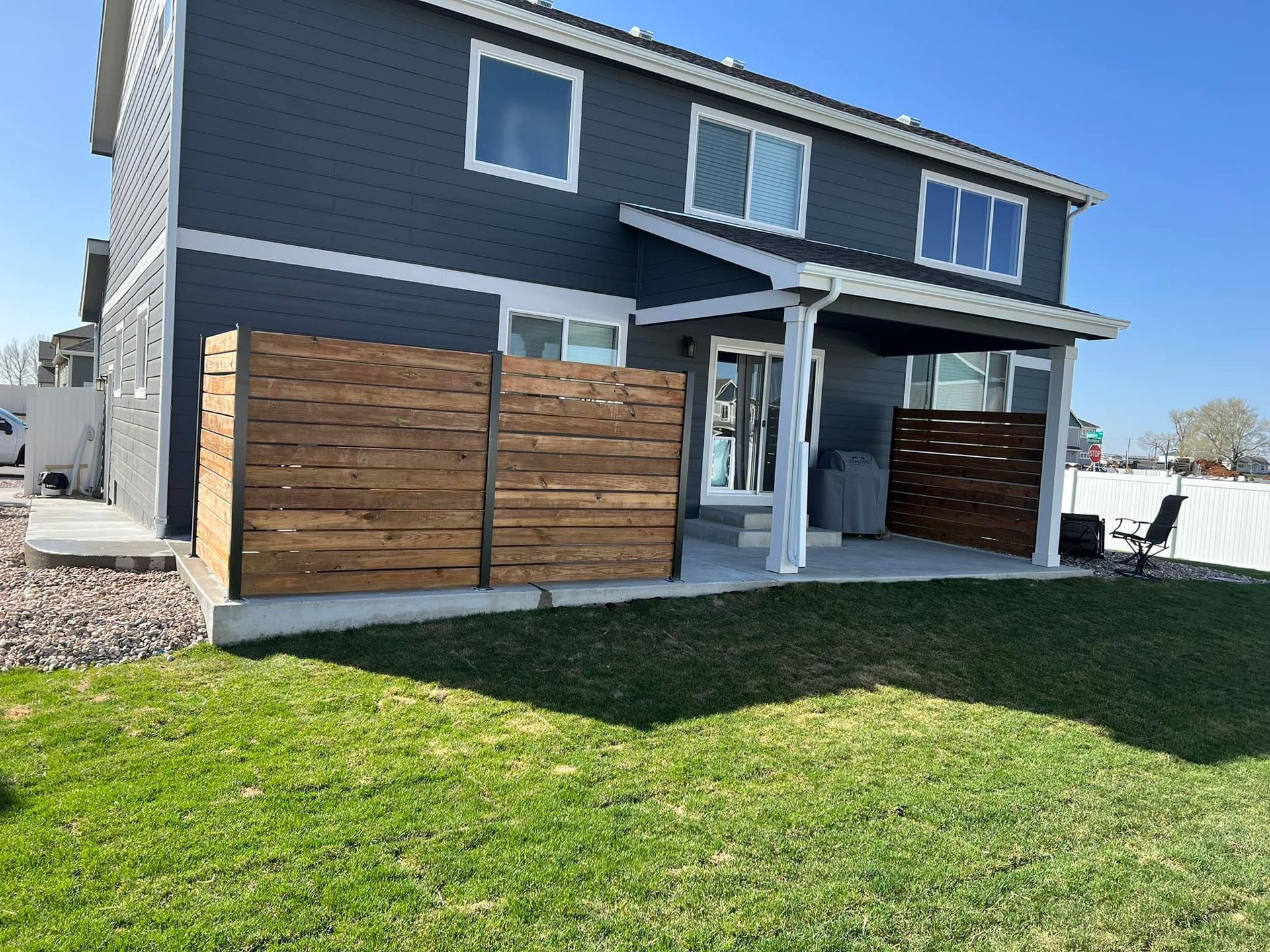 Backyard with two-story gray house, patio with pergola, wooden privacy fences, and green grass.