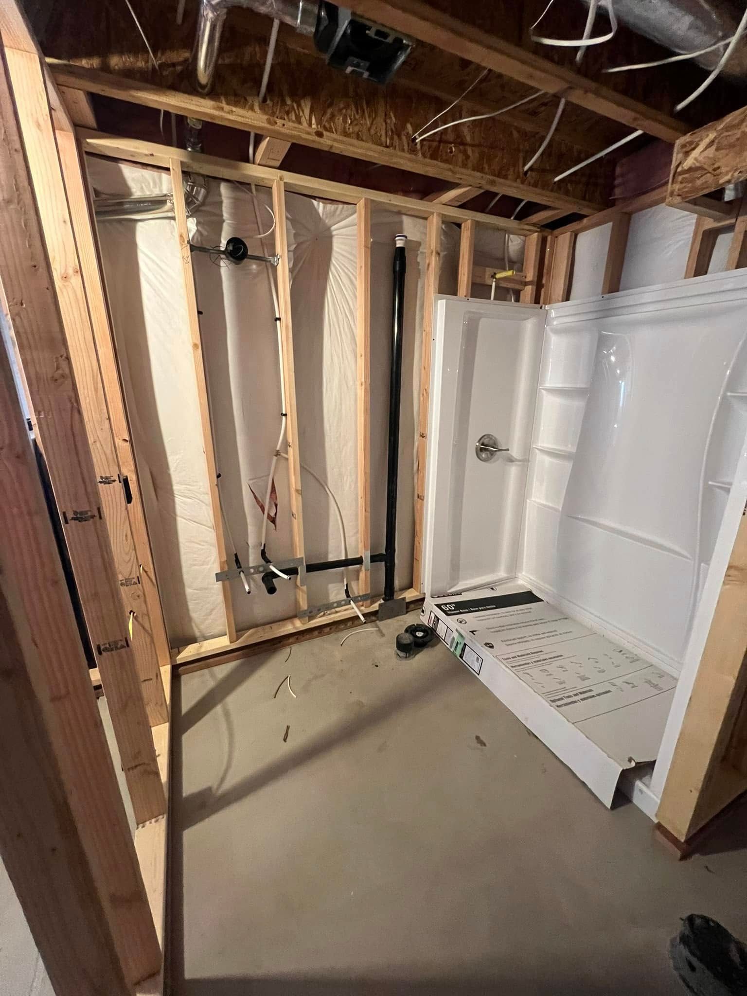 Framed walls with plumbing and a white shower stall in a basement.