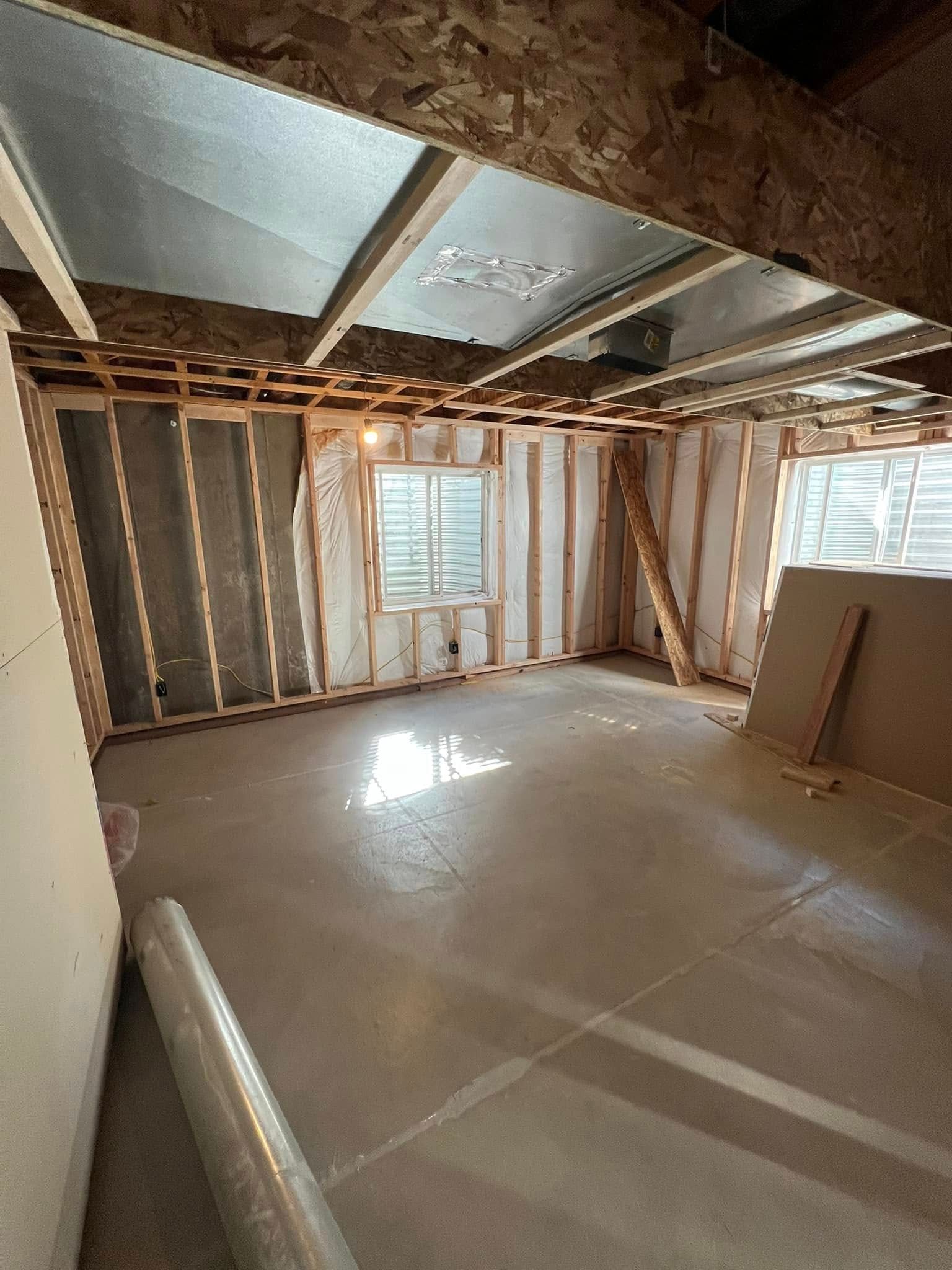 Unfinished basement with concrete floor, framed walls, windows, and exposed ceiling beams.