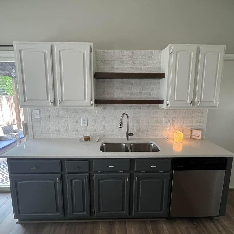Kitchen with white and gray cabinets, stainless steel sink, and floating wooden shelves.