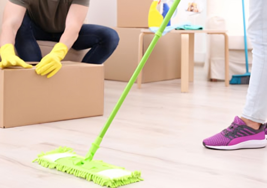 A man is sitting on a box while a woman is mopping the floor.
