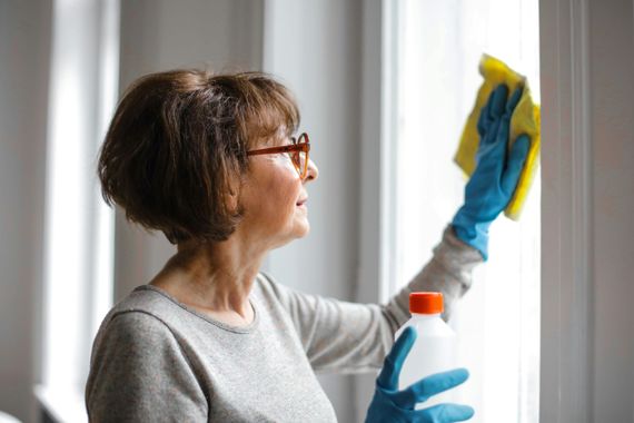 A woman is cleaning a window with a sponge and a bottle of cleaner.
