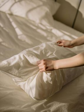 A person is making a bed with white sheets and pillows.