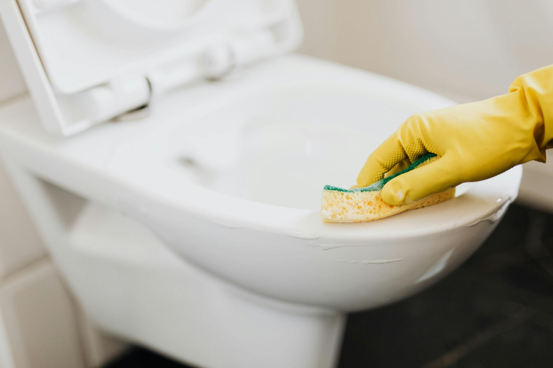 A person wearing yellow gloves is cleaning a toilet with a sponge.