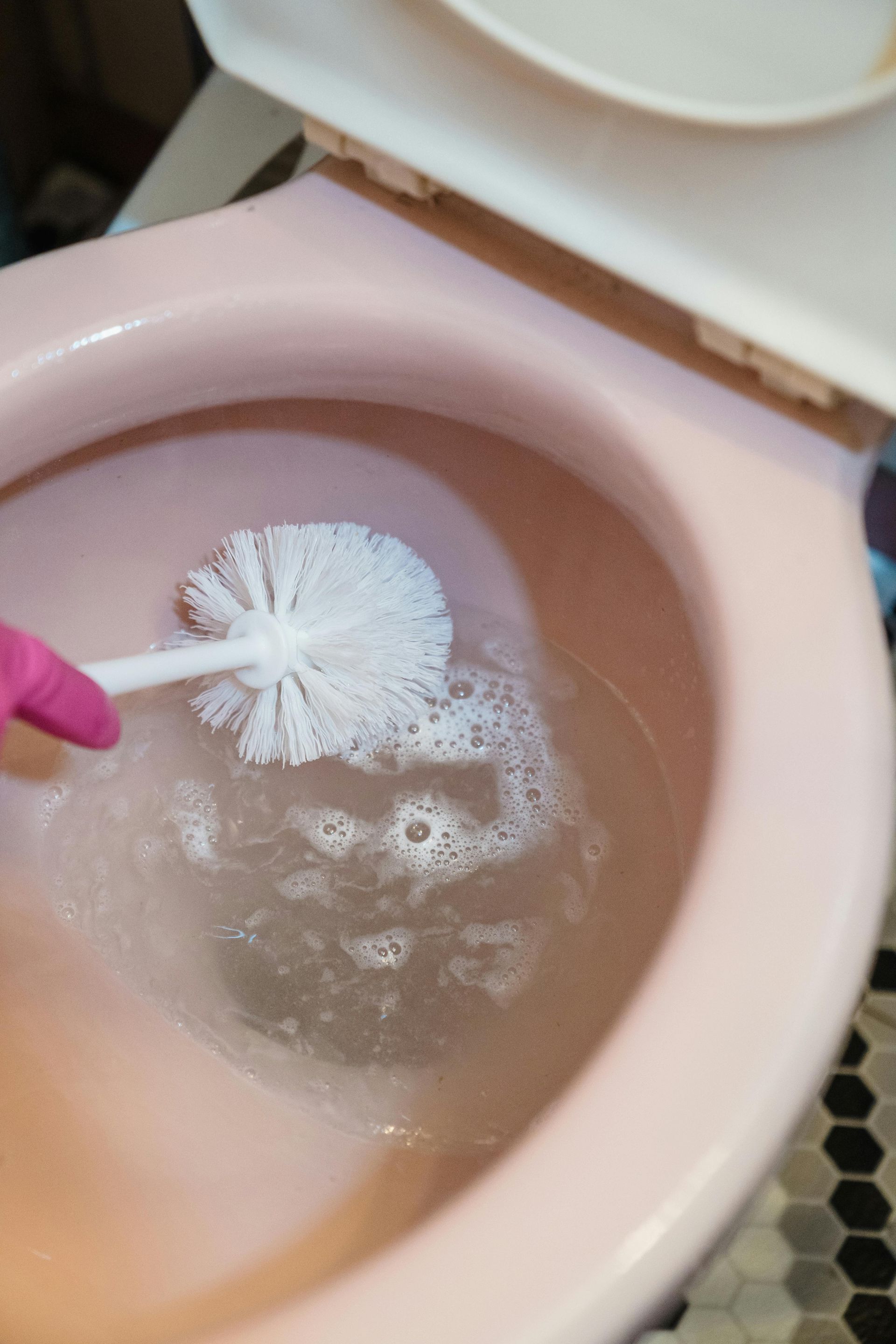 A person is cleaning a pink toilet with a toilet brush.