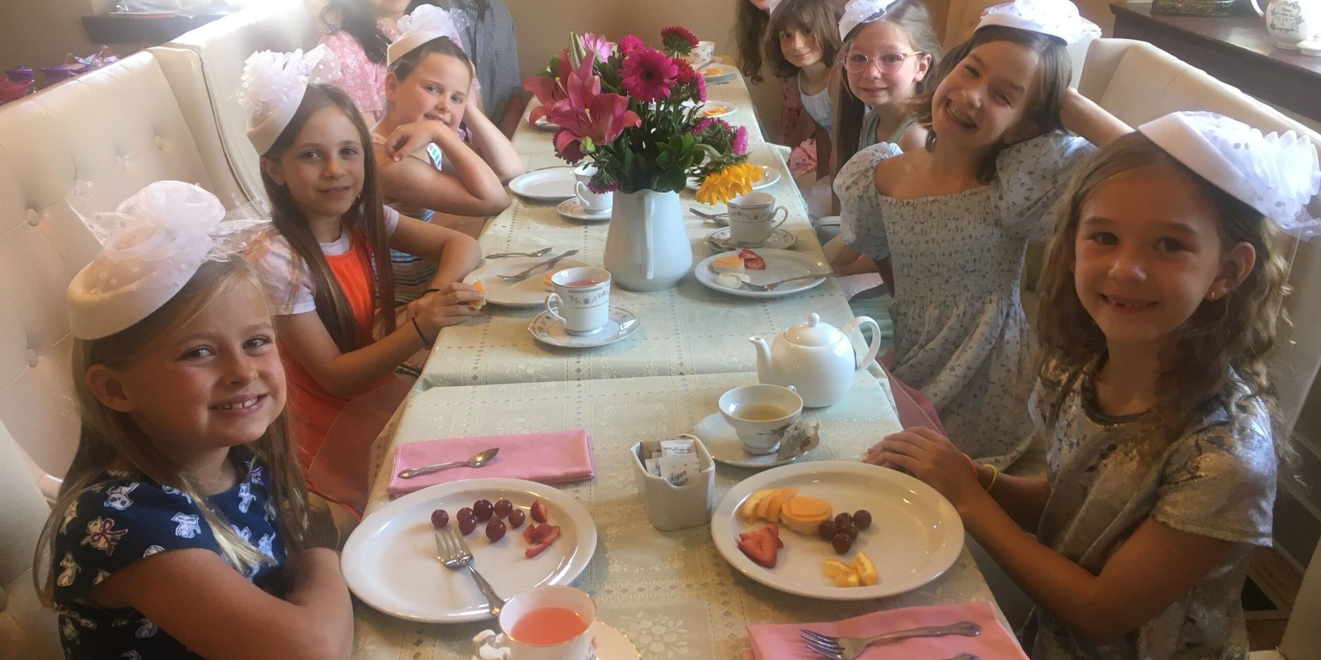 A group of young girls are sitting at a table with plates of food.