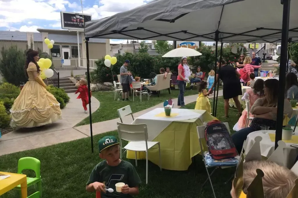 A group of children are sitting at tables under a tent at a birthday party.