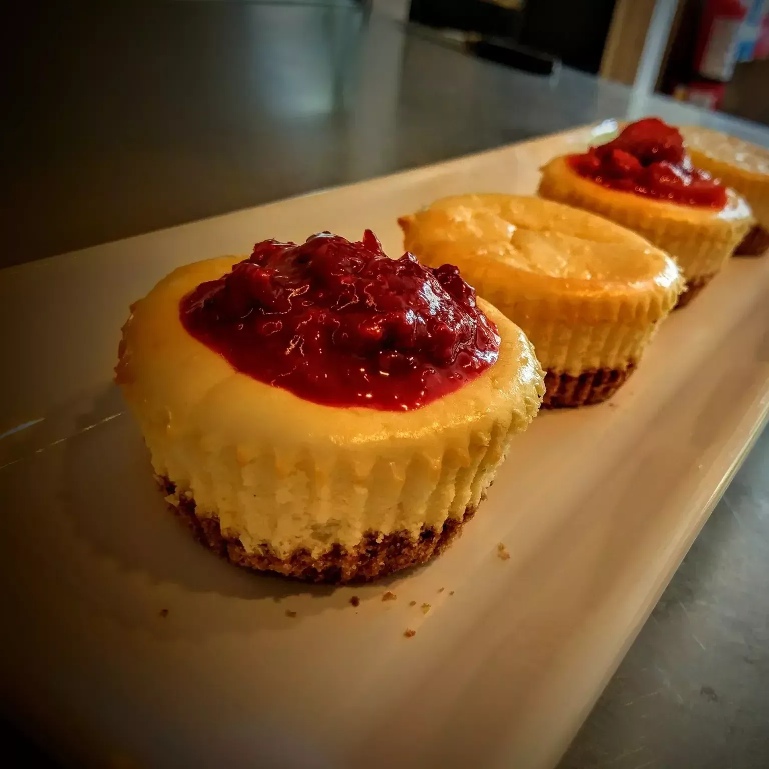 A row of cheesecake cupcakes with raspberry sauce on a white plate.