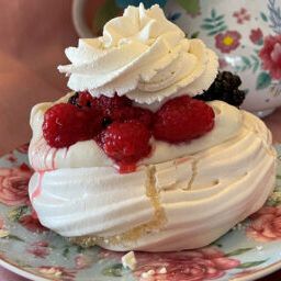A meringue cake with whipped cream and raspberries on a plate.