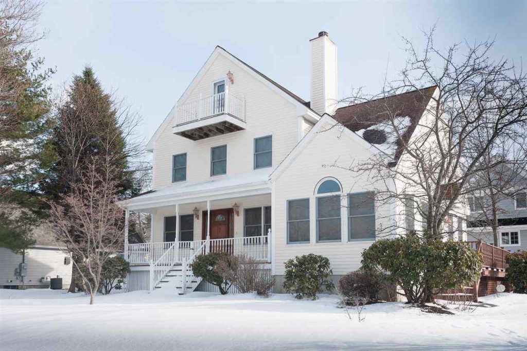 A large white house with a large porch is covered in snow.