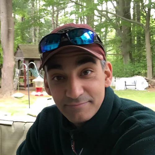 A man wearing a hat and sunglasses is smiling for the camera