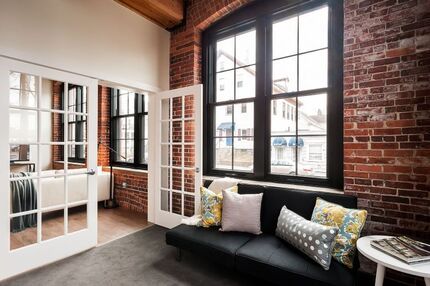 A living room with a black couch and a brick wall.