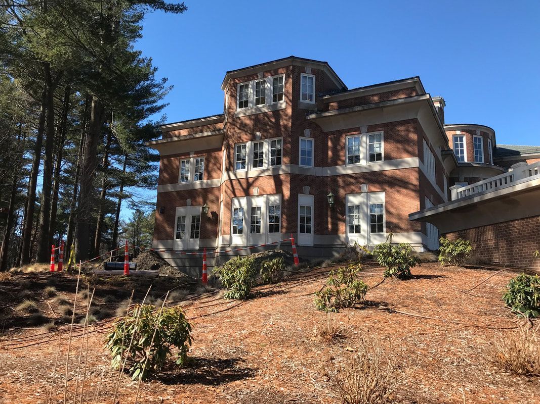A large brick building is sitting on top of a hill surrounded by trees.