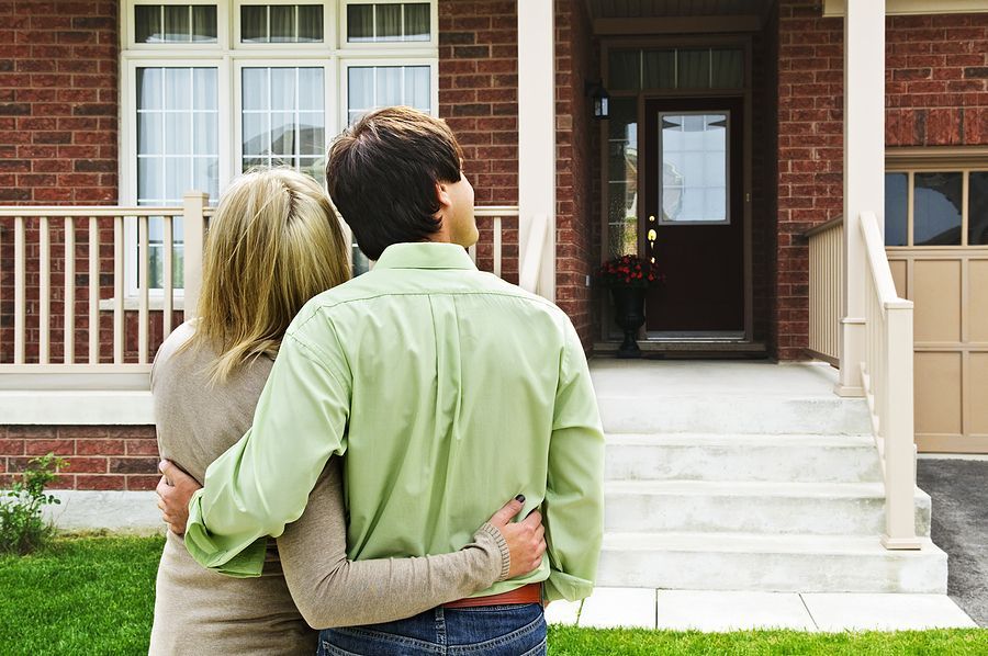 A man and woman are hugging in front of a brick house.