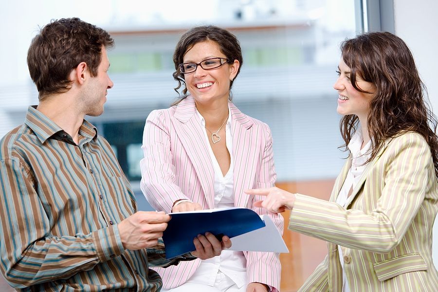 A man and two women are talking to each other while a woman points at a clipboard.