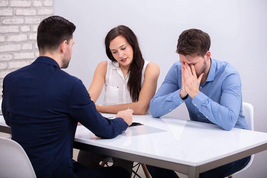 A man and a woman are sitting at a table talking to a man.