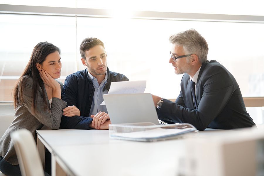 A man and a woman are sitting at a table looking at a laptop.