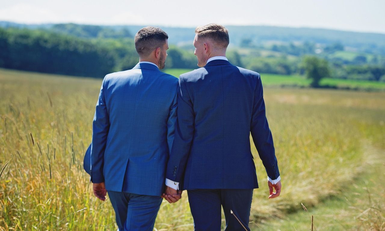 Two men in suits are walking through a field holding hands.