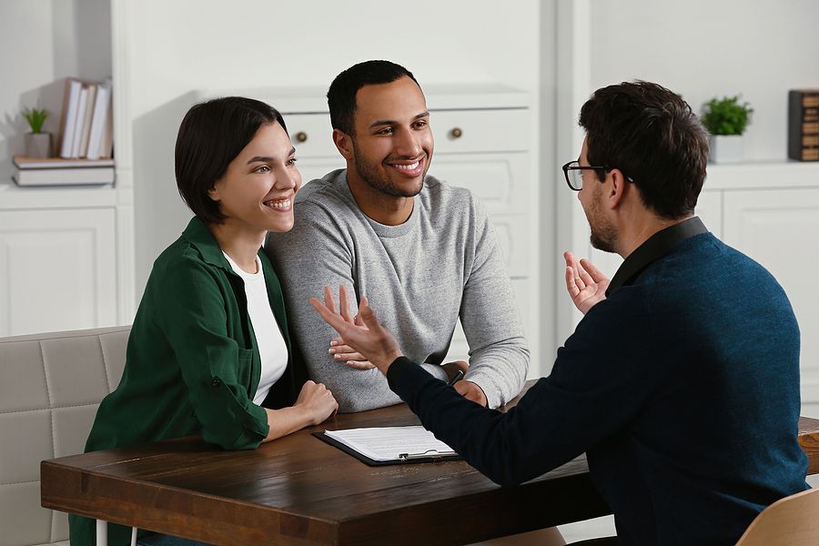 A man and woman are sitting at a table talking to a real estate agent.