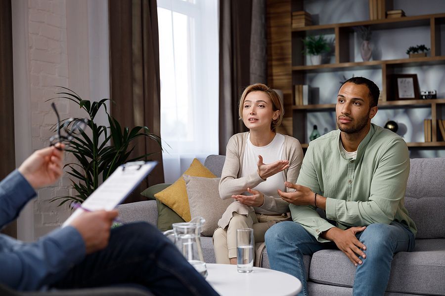 A man and a woman are sitting on a couch talking to a counselor.