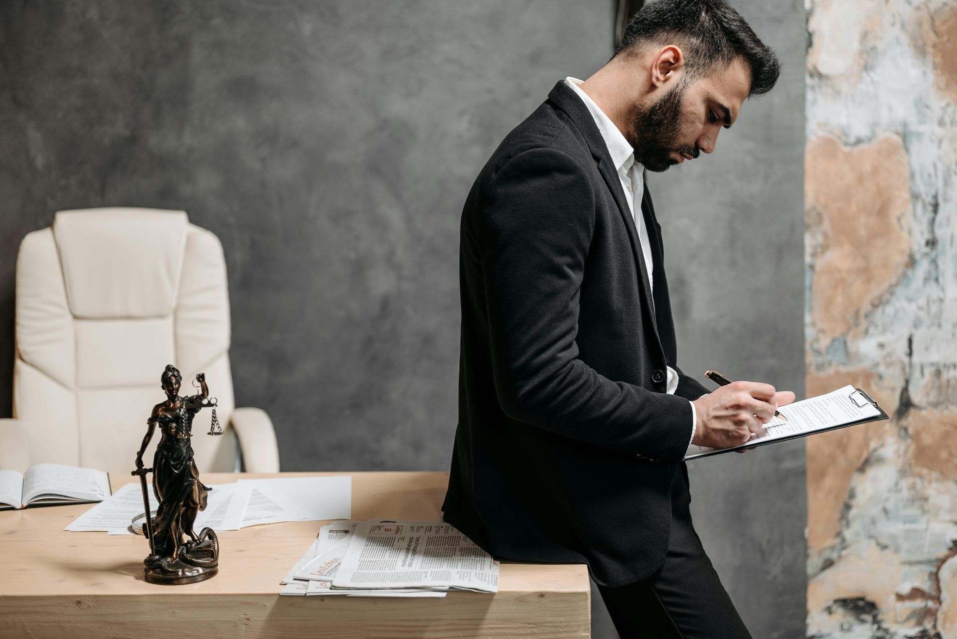 A man in a suit is sitting at a desk writing on a clipboard.