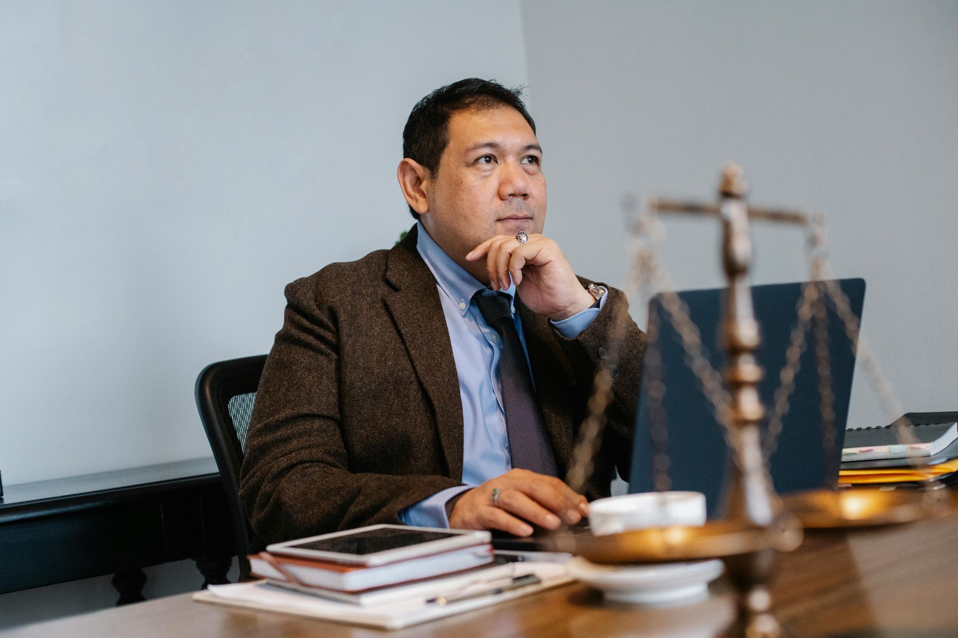 A man in a suit and tie is sitting at a desk in front of a laptop computer.
