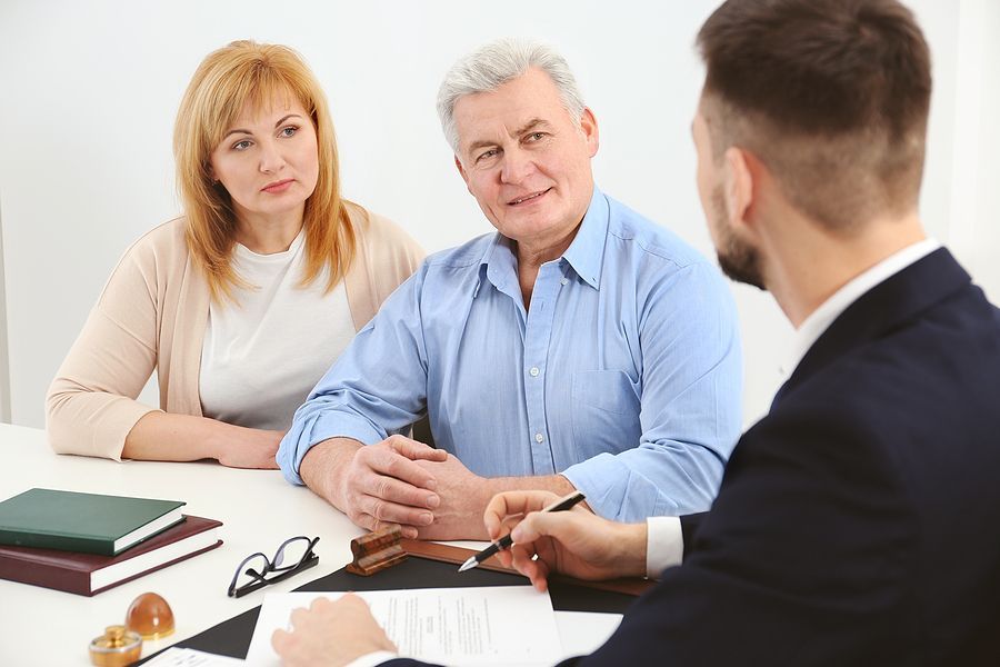 A man and a woman are sitting at a table talking to a man.