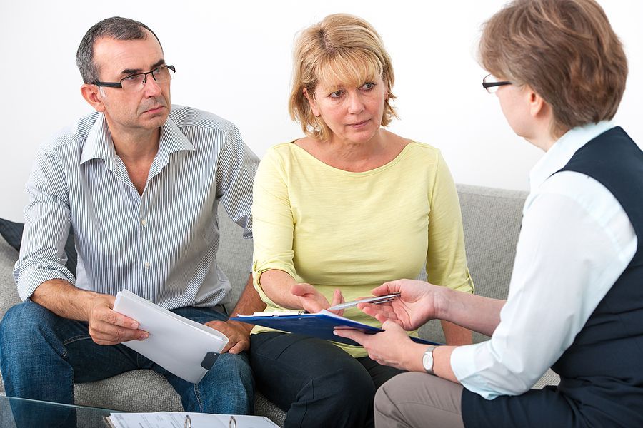 A man and a woman are sitting on a couch talking to a woman.